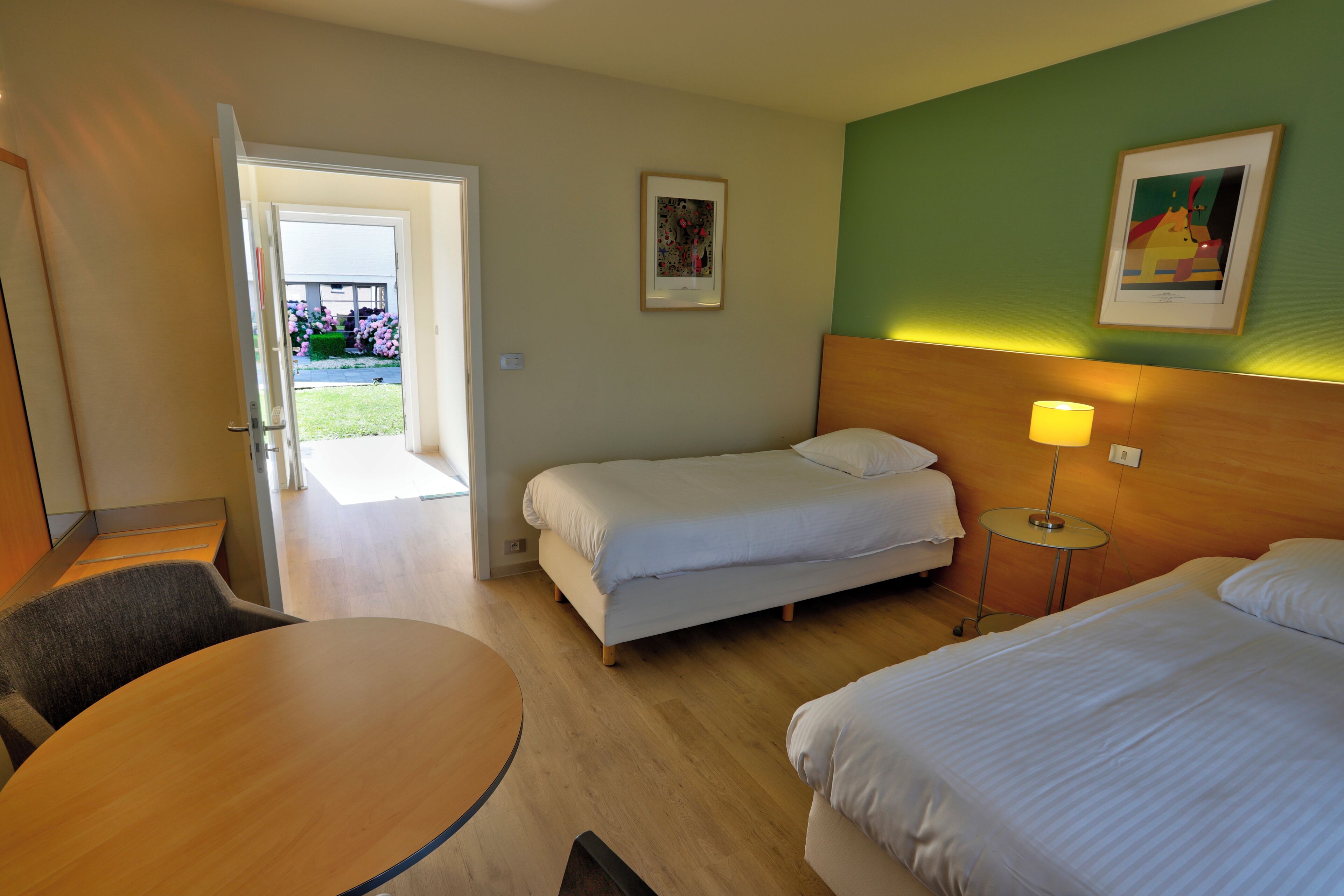 A hotel room with a bed, a chair, a table, and a door leading to a balcony.