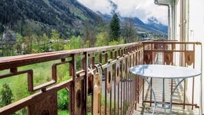 Ein Balkon mit Metallgeländer, Tisch und Stühlen, mit Blick auf eine gebirgige Landschaft und ein Dorf darunter.