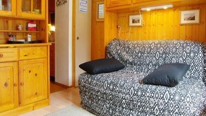 Ein gemütliches Zimmer mit einer gemusterten Couch, Holzelementen und einer Tür zu einem weiteren Raum.