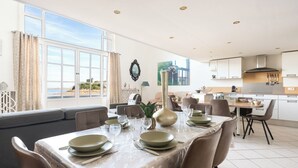 A modern dining area with a table set for four, a sofa, and a view of the sea. - La Plage by Interhome (Dinard)