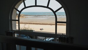 A view through a window with a semi-circular arch, overlooking a beach with sand, sea, and distant landforms. - La Plage by Interhome (Dinard)