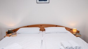 Un lit double avec du linge de lit blanc, deux oreillers, une tête de lit en bois et des tables de chevet avec des lampes et des livres.