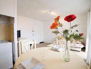 A modern living room with a dining table, a sofa, and a vase with flowers.