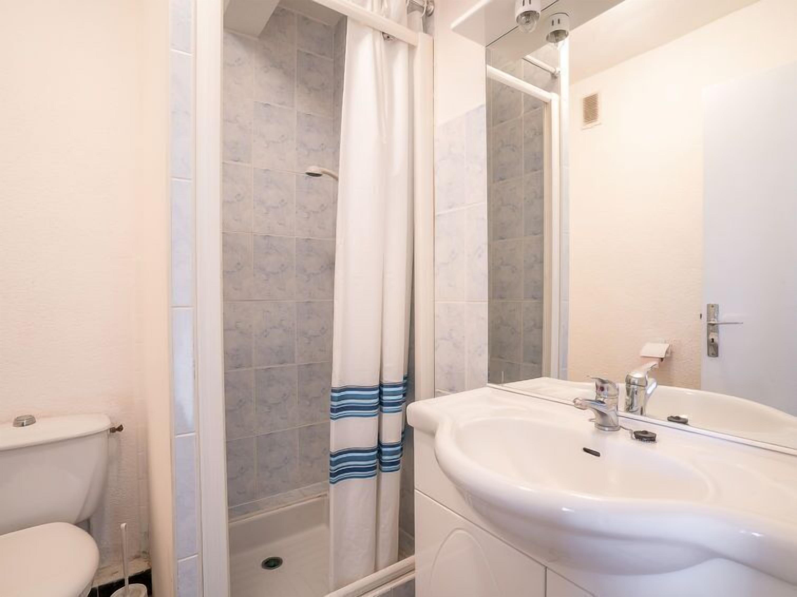 A bathroom with a toilet, a shower with a curtain, and a sink with a mirror.