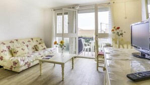 A living room with a sofa, coffee table, and a TV. There is a balcony with chairs and a table. - Les Amandiers by Interhome (Canet-Plage)