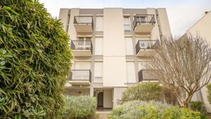 A multi-story residential building with balconies, a central entrance, and a garden area with various plants. - Les Amandiers by Interhome (Canet-Plage)