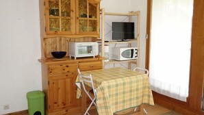 A compact kitchen with wooden cabinets, a microwave, a television, and a small dining table with a checkered tablecloth.