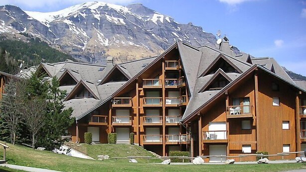 A multi-story lodge with a sloped roof, wooden balconies, and a mountainous backdrop.