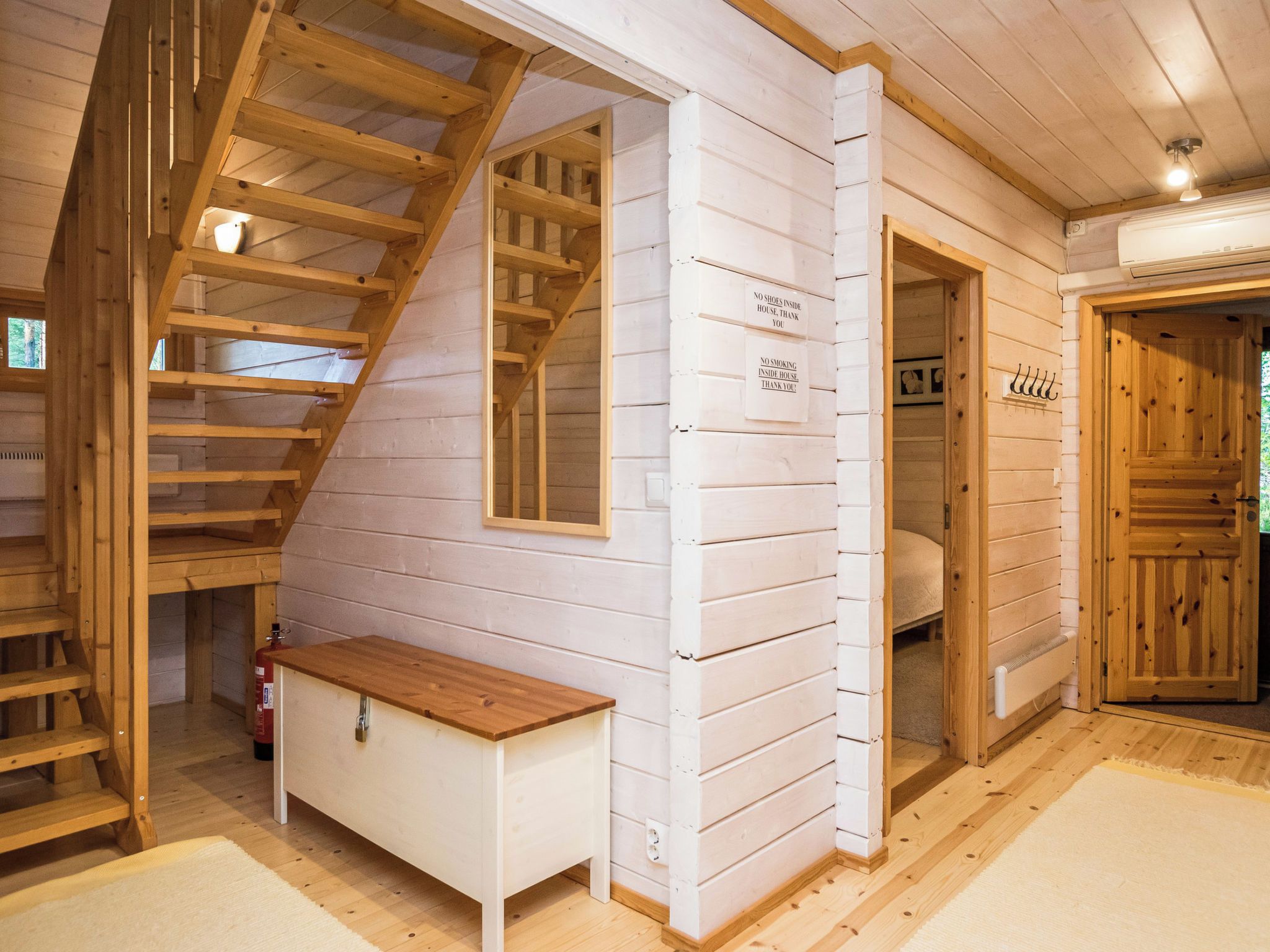 A wooden interior with a staircase, a bench, and a door with a sign.