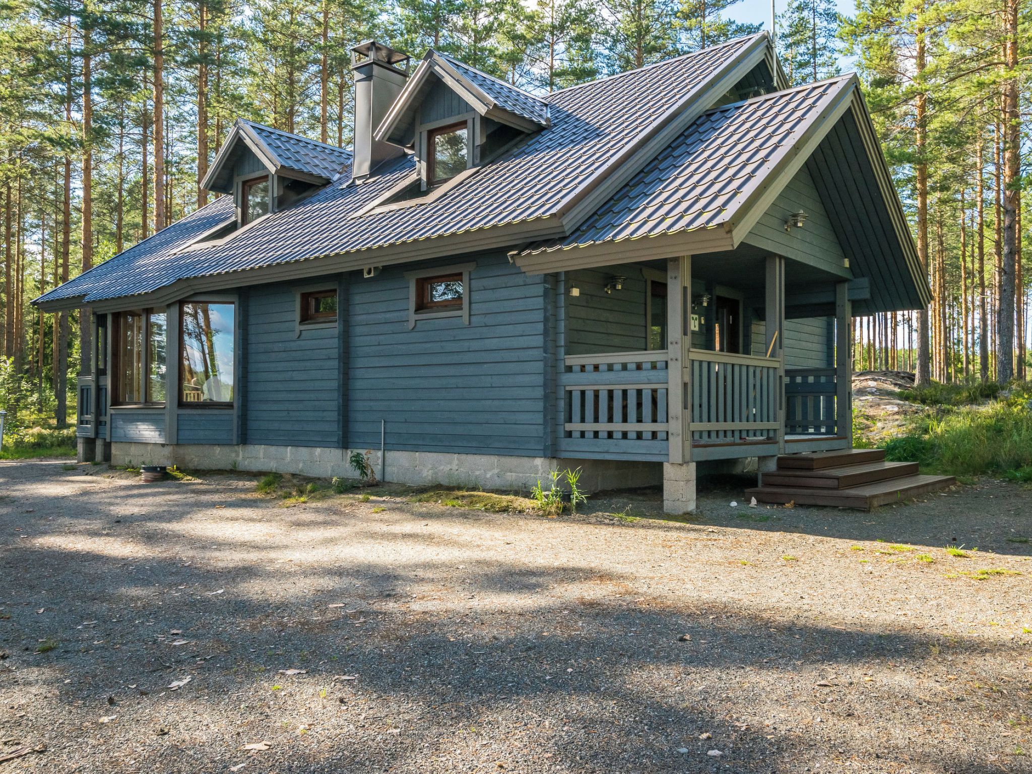 A cabin with a porch, a chimney, and a gravel driveway.