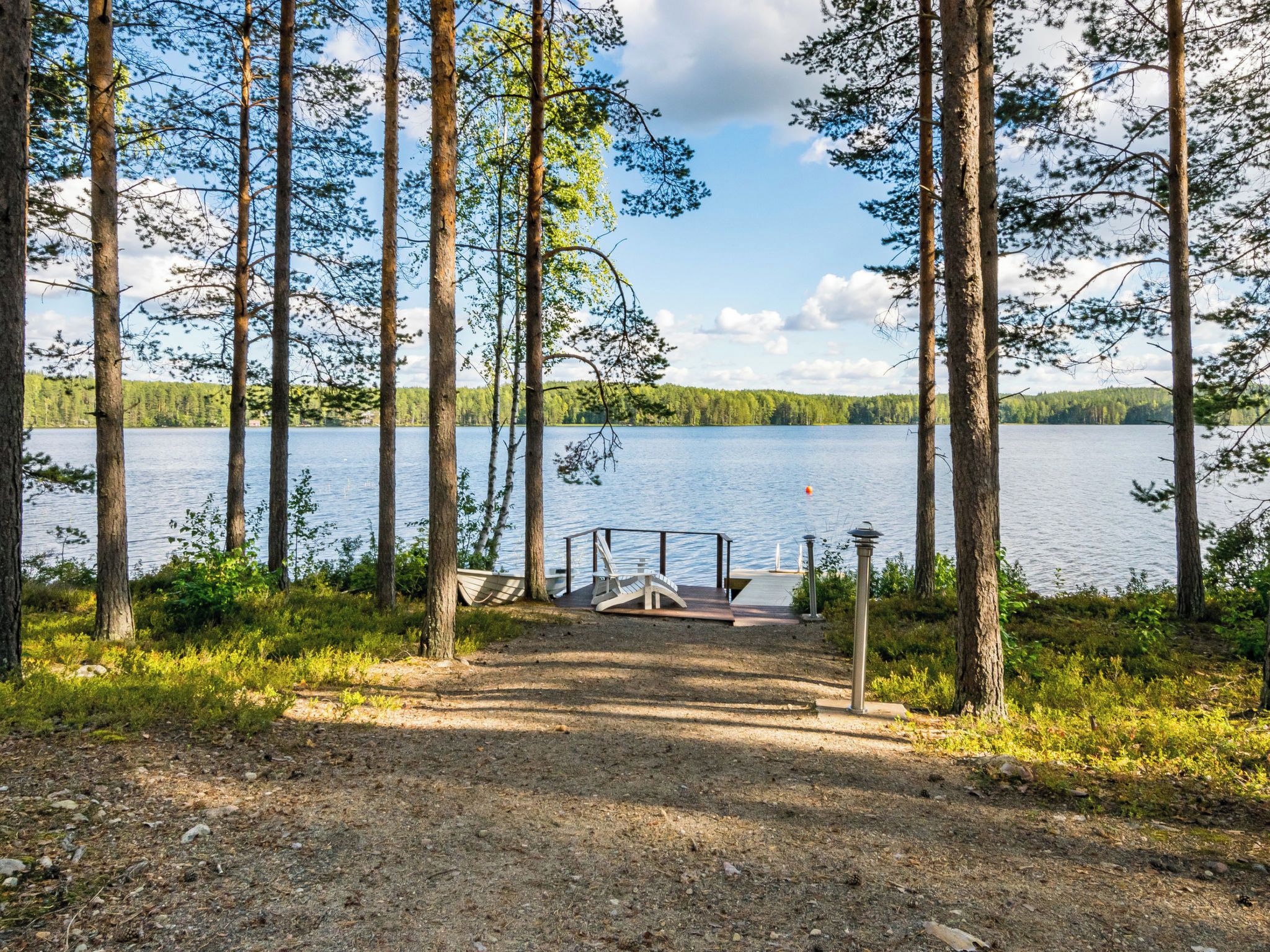 Terassi järven rannalla, josta avautuu näkymä tyynelle järvelle, ja terassin ympärillä kohoaa korkeita puita.
