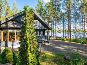Eine Hütte mit Veranda, umgeben von Bäumen und einem See.