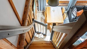 Una escalera de madera con barandillas de metal que conduce a una habitación con una mesa y sillas de madera.