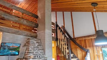 A wooden interior with a stone fireplace, wooden staircase, and a hanging light fixture.