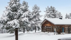Una cabaña rústica de troncos con techo nevado, rodeada de árboles cubiertos de nieve.