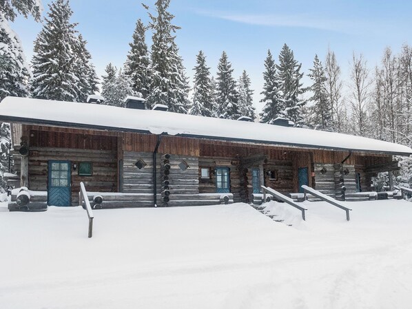 A log cabin with a snow-covered roof and wooden walls, surrounded by snow-covered trees.