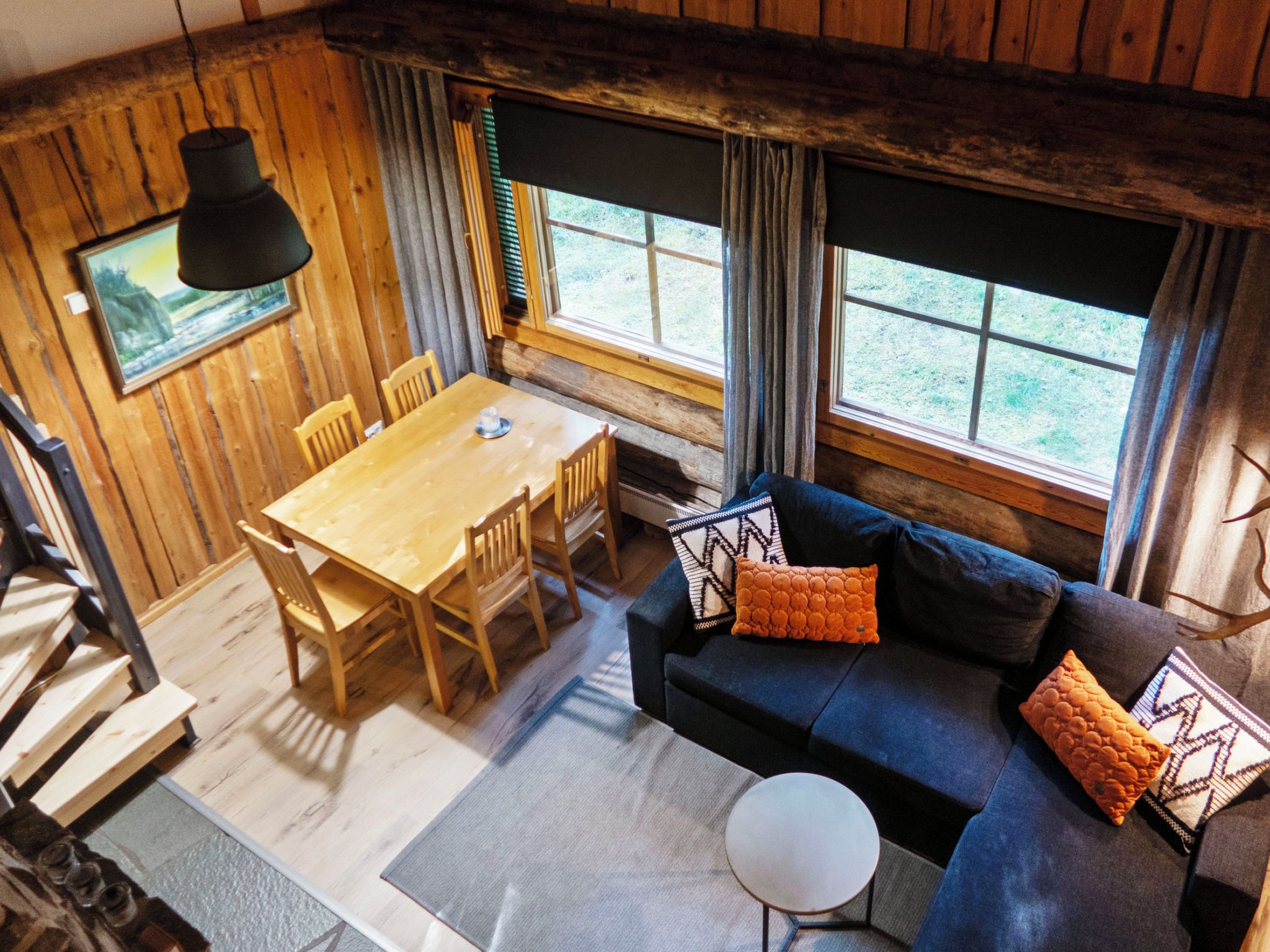 Une pièce chaleureuse avec un décor intérieur en bois, une table à manger avec des chaises, un canapé avec des coussins et une fenêtre avec des rideaux.