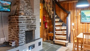 Un interior rústico con chimenea de piedra, escalera de madera y comedor con mesa y sillas.