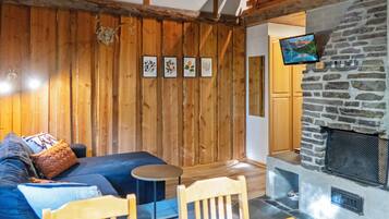 A cozy room with a stone fireplace, wooden walls, a sofa, and a television mounted above the fireplace.