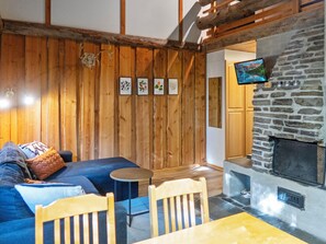 A cozy room with a stone fireplace, wooden walls, a sofa, and a television mounted above the fireplace.