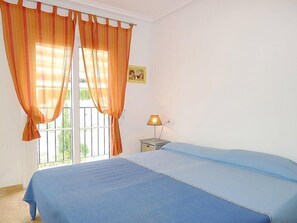 Une chambre avec un lit, une table de chevet, une lampe et une fenêtre avec des rideaux.