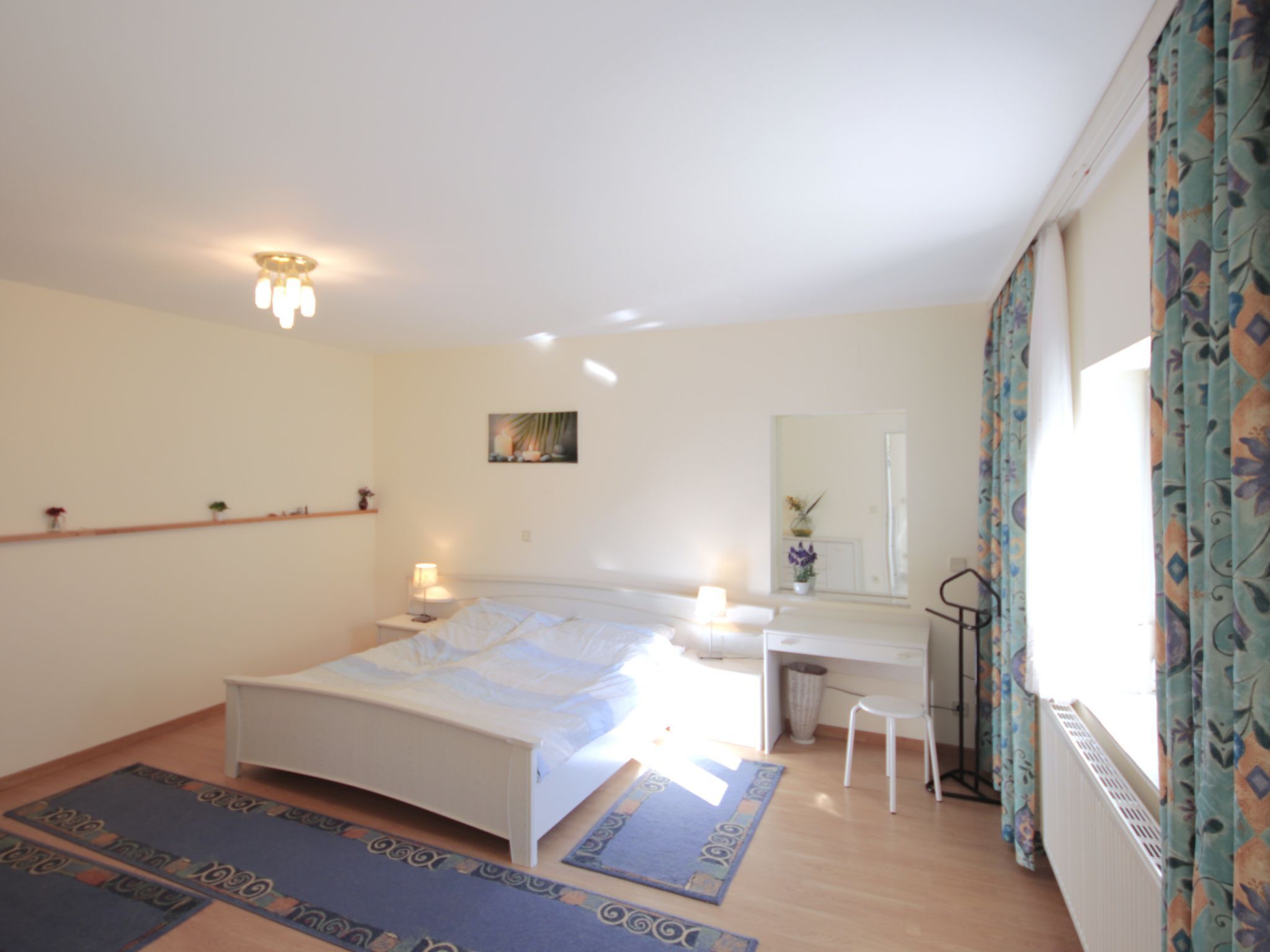 Une chambre à coucher comprenant un lit, une table de chevet, un bureau, une chaise et une fenêtre avec des rideaux.