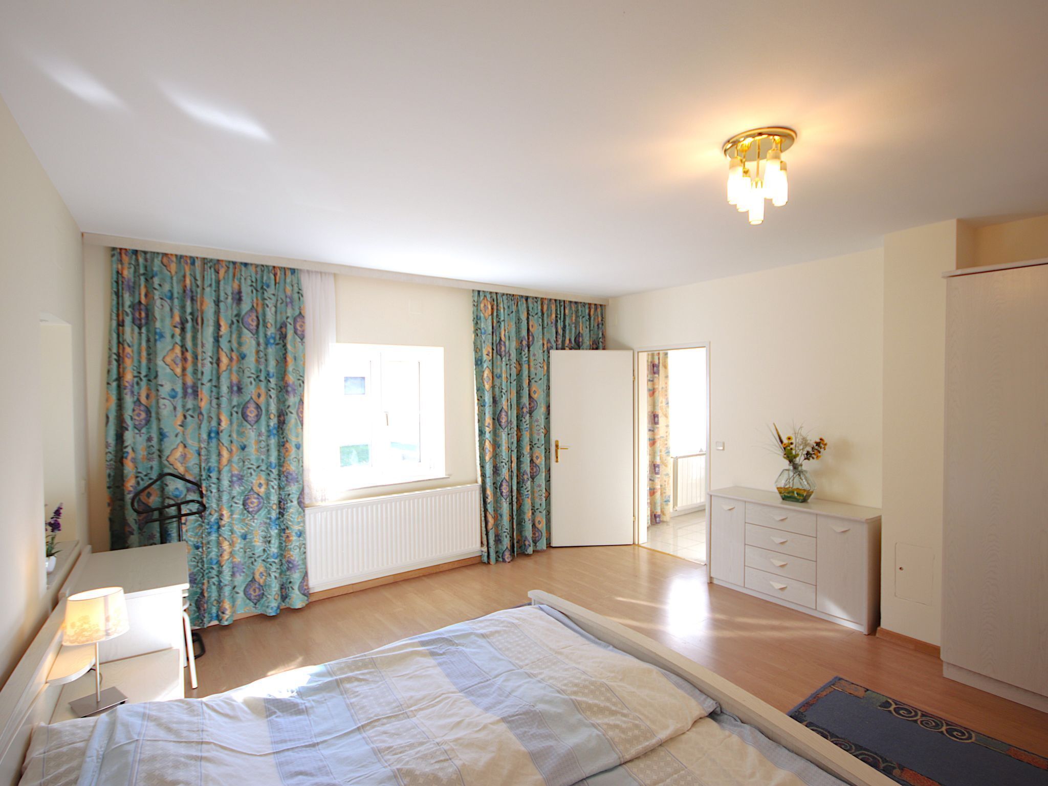 Une chambre à coucher avec un lit, un bureau, une commode et une fenêtre avec des rideaux.