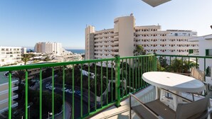A balcony with a green railing overlooking a coastal cityscape, featuring a dining area with a table and chairs. - Apartamentos Don Diego (San Bartolomé de Tirajana)
