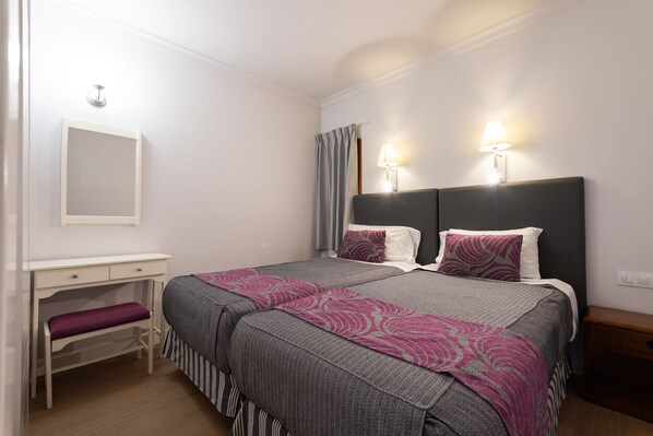 Un dormitorio ordenado con una cama doble, lámparas de noche, un escritorio con una banqueta y un espejo en la pared.
