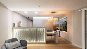 A modern hotel lobby with a reception desk, a sofa, a dining area, and a large window offering a view. - Apartamentos Don Diego (San Bartolomé de Tirajana)