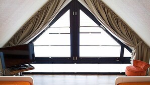 A cozy room with a large window, a flat-screen TV, two orange chairs, and a decorative rug.
