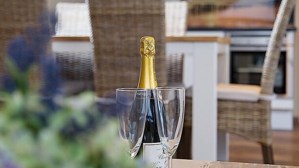 A bottle of champagne in a glass on a table with wicker chairs in a modern interior setting.