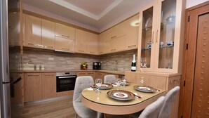 A modern kitchen with wooden cabinets, a built-in oven, and a dining area with a glass table set for four. - Sea Front Panorama Villa Private Pool (Malevizi)