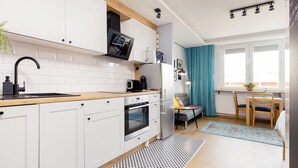 Ett modernt kök med vita skåp, en träbänkskiva och en inbyggd ugn. Det finns en matplats med ett bord och stolar, och ett fönster med gardiner.
