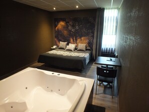 A bedroom with a large bed, a desk, and a bathtub. - Motel Los Abedules (Oviedo)