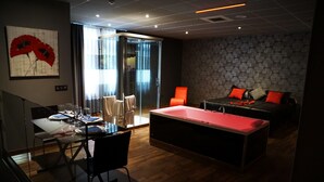 A modern hotel room with a dining area, a red pool table, and a bedroom with a large bed and red pillows. - Motel Los Abedules (Oviedo)