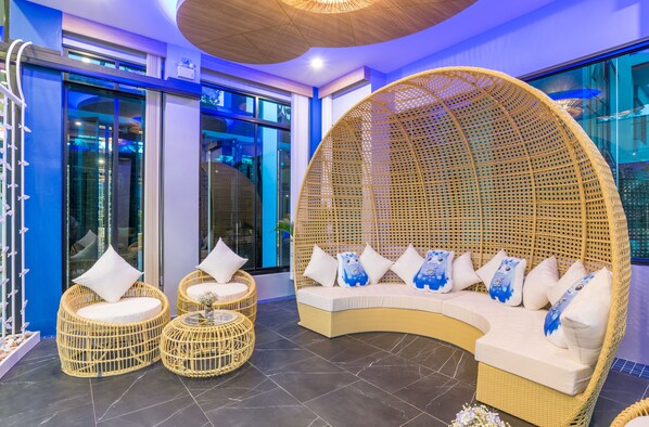 A modern lounge area with wicker furniture, including a large curved sofa and two round chairs, and a decorative wicker structure. - Anda Sea Tales Resort (Krabi)