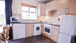 A compact kitchen with a washing machine, microwave, oven, and a refrigerator. - Upton Court Holiday Cottages (Kilmuckridge)