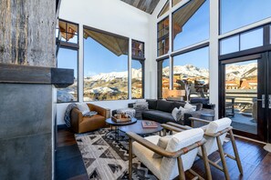 A modern living room with large windows, a sofa, a coffee table, and a view of snow-capped mountains.