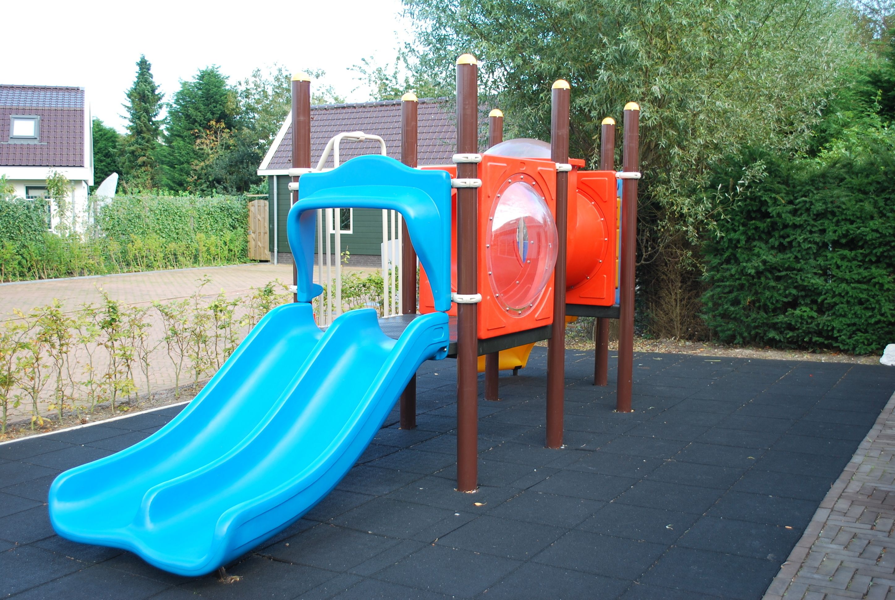 Een speeltuin met een blauwe glijbaan en een rode, ronde klimstructuur.