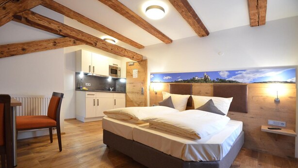A bedroom with a bed, a chair, a nightstand, a wall-mounted lamp, and a view of the sky. - BAUER Gästezimmer (Kipfenberg)