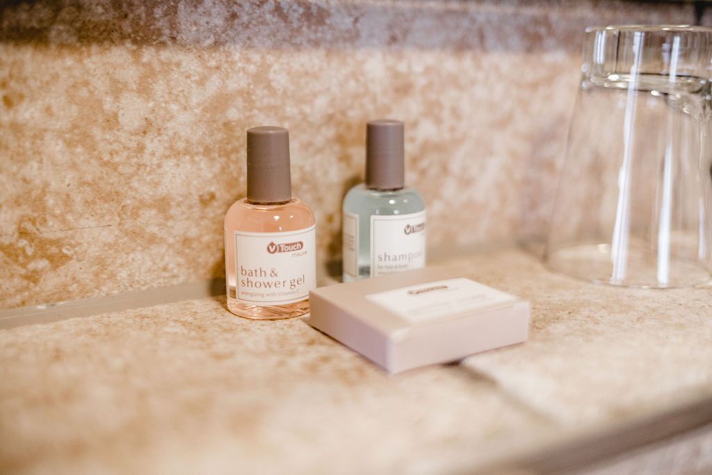 Un meuble-lavabo de salle de bain avec un plan de toilette en marbre, deux flacons de gel douche de la marque Touch et un verre transparent.
