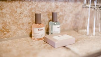 Un meuble-lavabo de salle de bain avec un plan de toilette en marbre, deux flacons de gel douche de la marque Touch et un verre transparent.