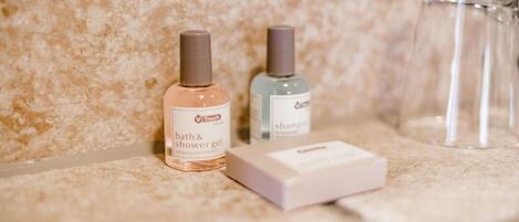 A bathroom vanity with a marble countertop, two bottles of Touch brand bath and shower gel, and a clear glass.