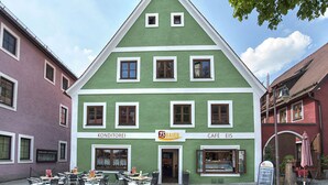 A green building with a sign for 'KONDITOREI' and 'BAUER CAFE EIS' on the ground floor. There are outdoor tables and chairs in front. - BAUER Gästezimmer (Kipfenberg)