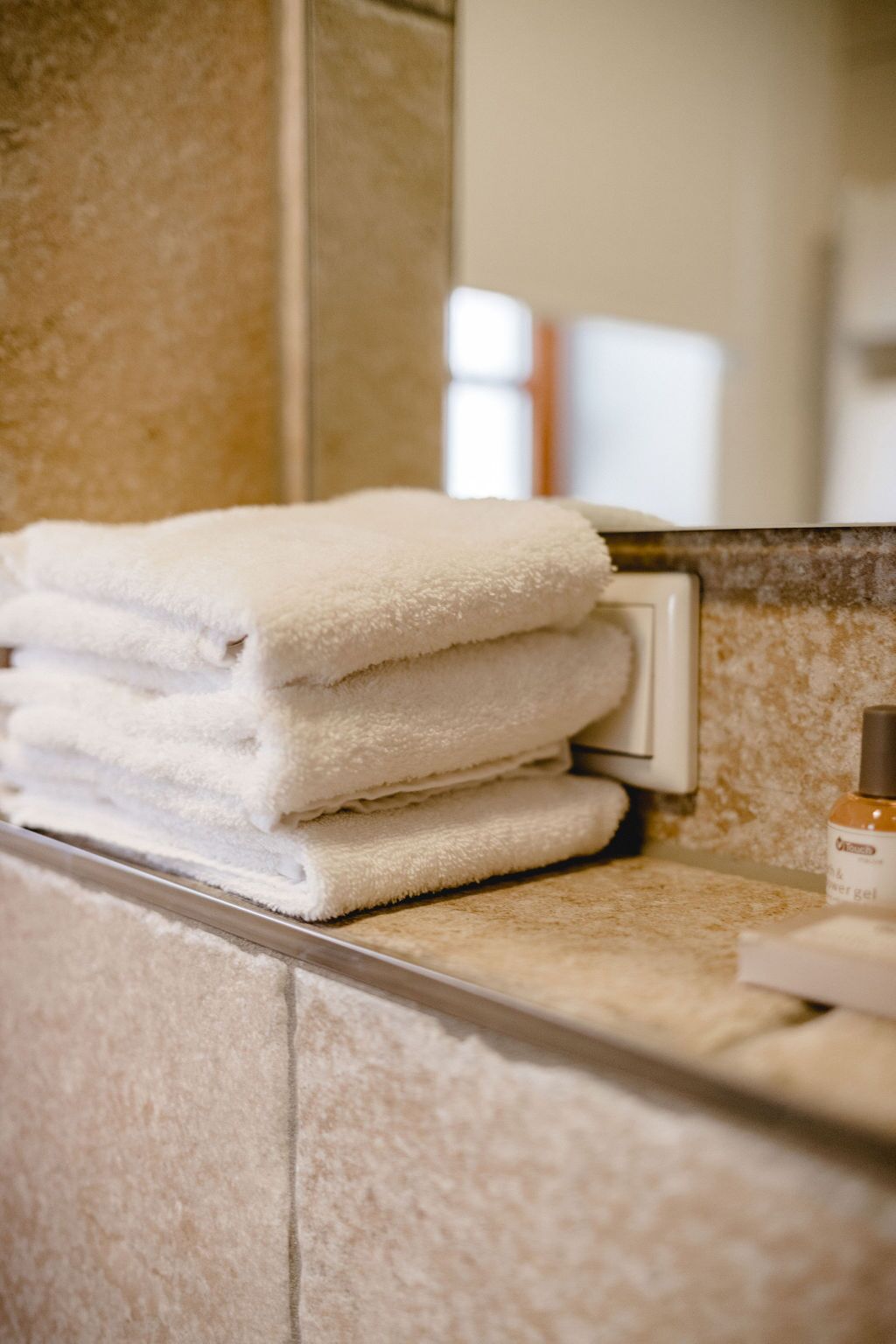 A stack of white towels on a bathroom counter with a bottle of lotion.