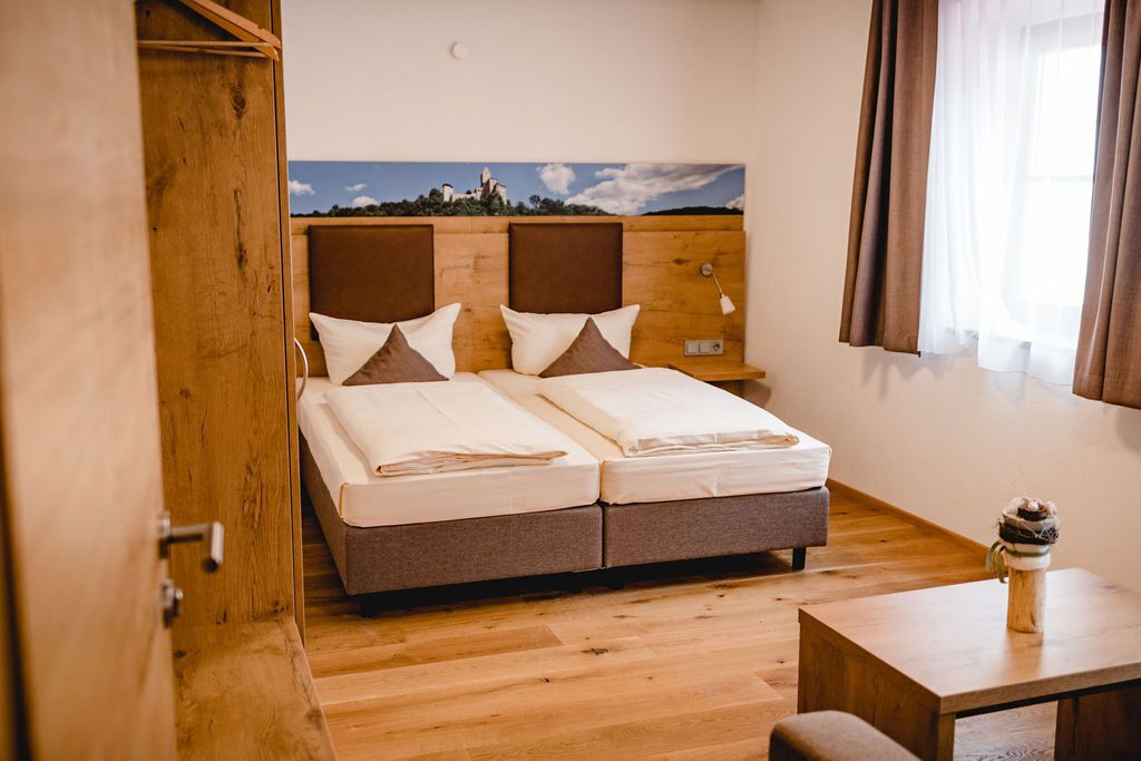 Una cama doble con cabecera de madera, una mesita de noche y vistas a un paisaje a través de una ventana con cortinas.