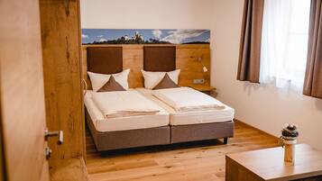 Una cama doble con cabecera de madera, una mesita de noche y vistas a un paisaje a través de una ventana con cortinas.