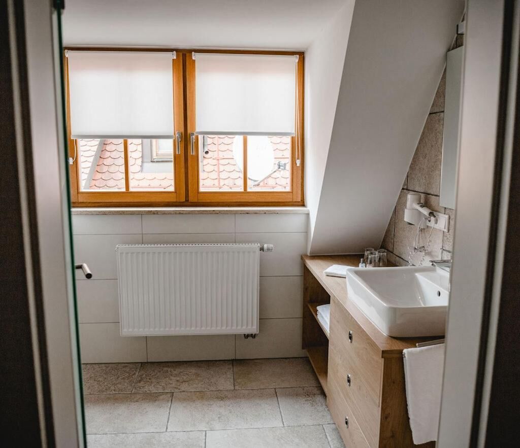 Un baño pequeño y moderno con ventana, radiador, lavabo y muebles de madera.