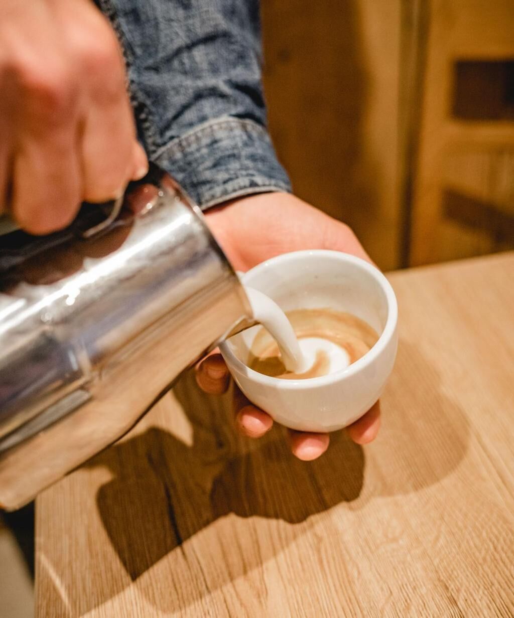 Una persona vertiendo leche en una taza de café.